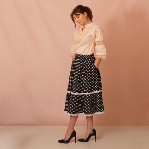 model wearing a flare black polka dot midi skirt adorned with bobbin lace and peach-coloured top also adorned with bobbin lace